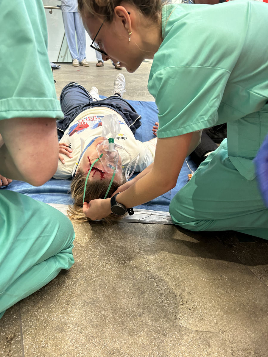 Eine Darstellerin liegt mit aufgeschminkter Kopfwunde am Boden, eine Studentin zieht ihr eine Sauerstoffmaske über.